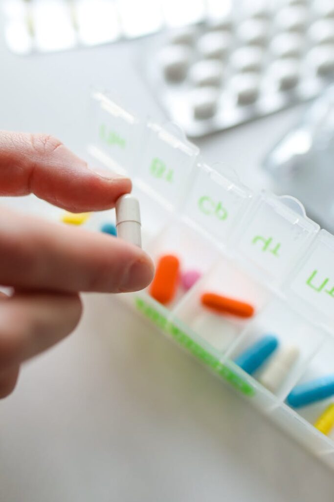 Hand holds a capsule near a colorful pill organizer, conveying medical organization.